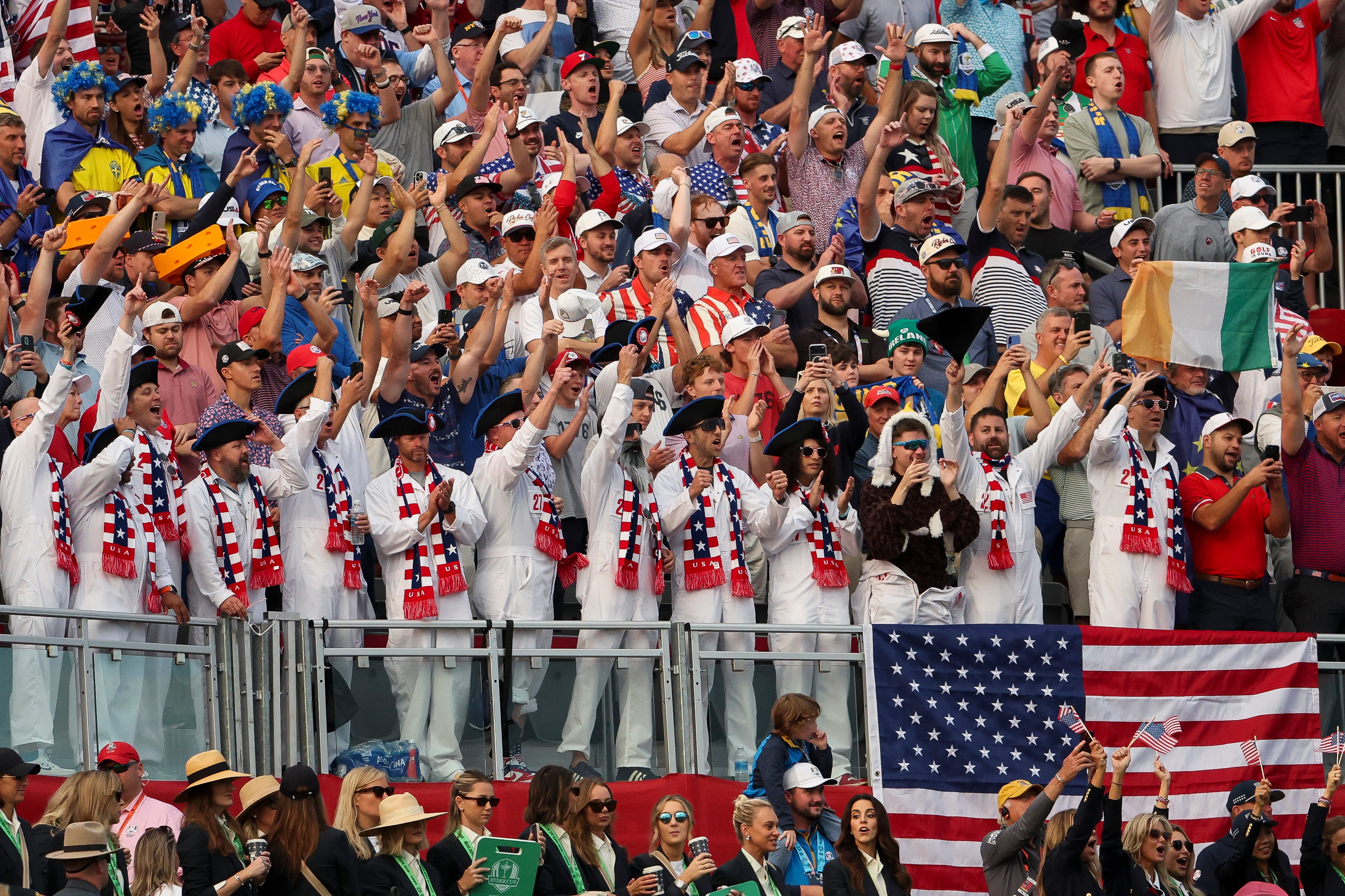 Crowd of diverse sports fans enthusiastically cheering at a stadium, some wearing white outfits and waving an American flag