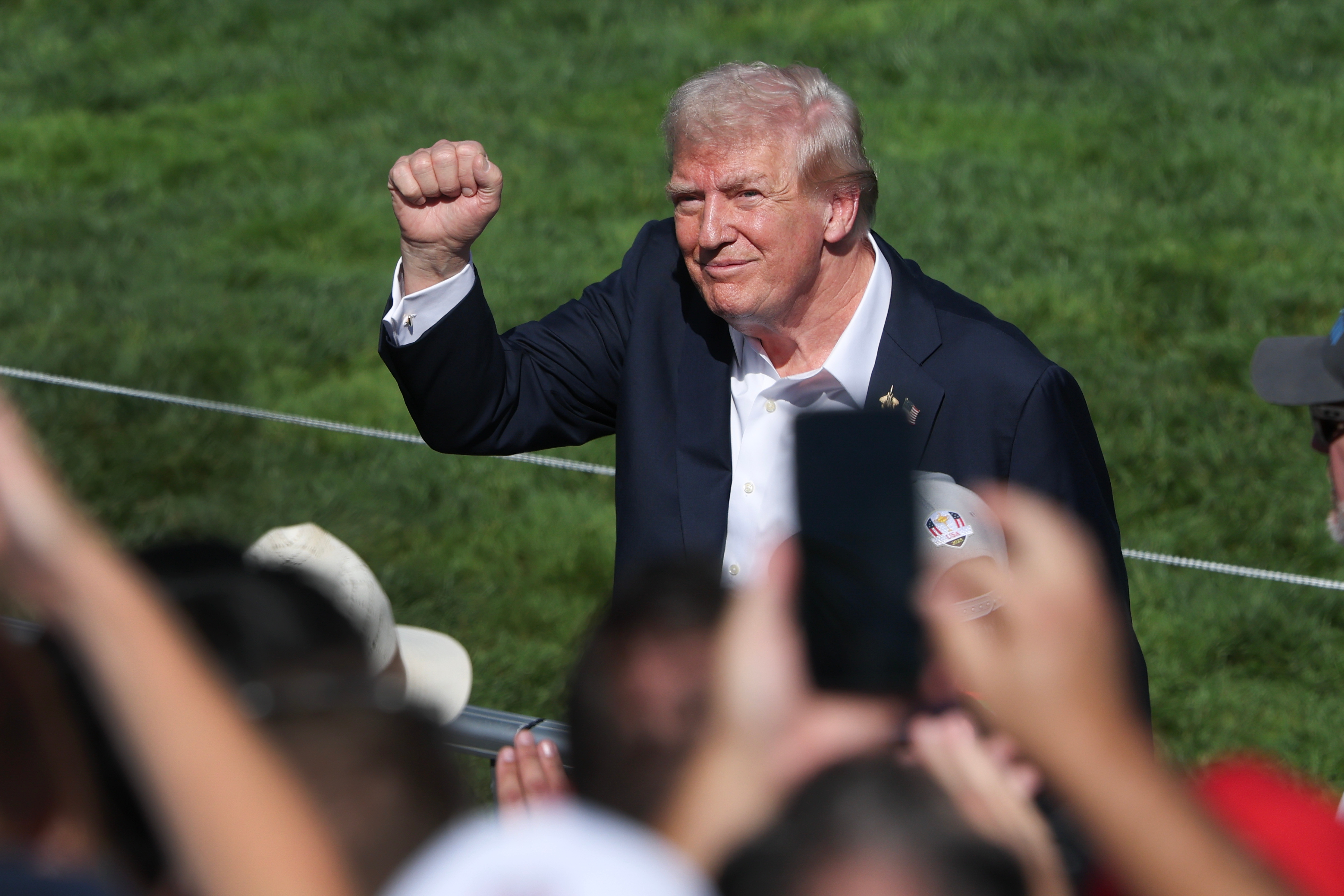 Individual in a suit raises a fist among a crowd at an outdoor event