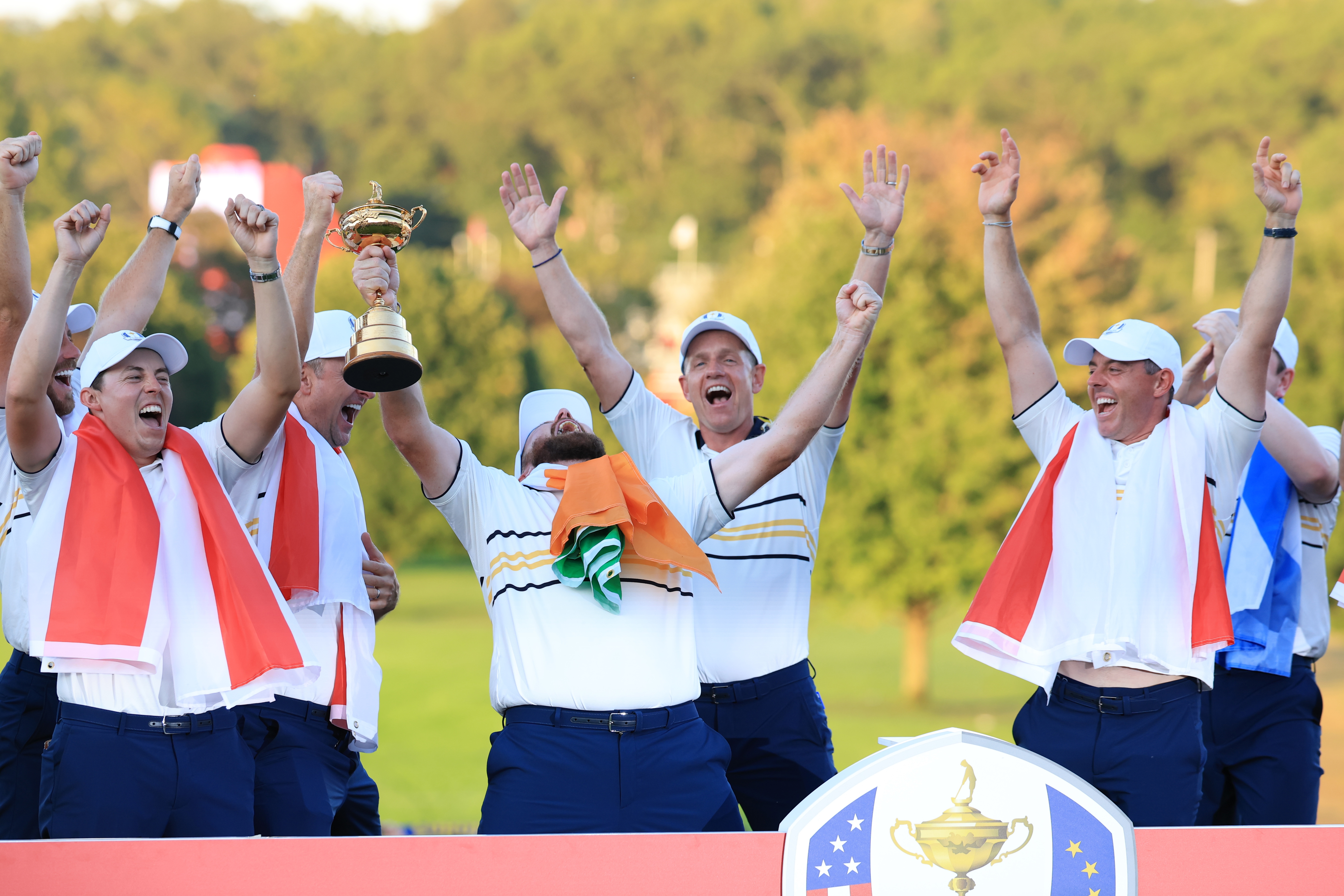 Golf team celebrating victory with a trophy, outdoors on a sunny day. Team members raise their arms and one holds the trophy aloft