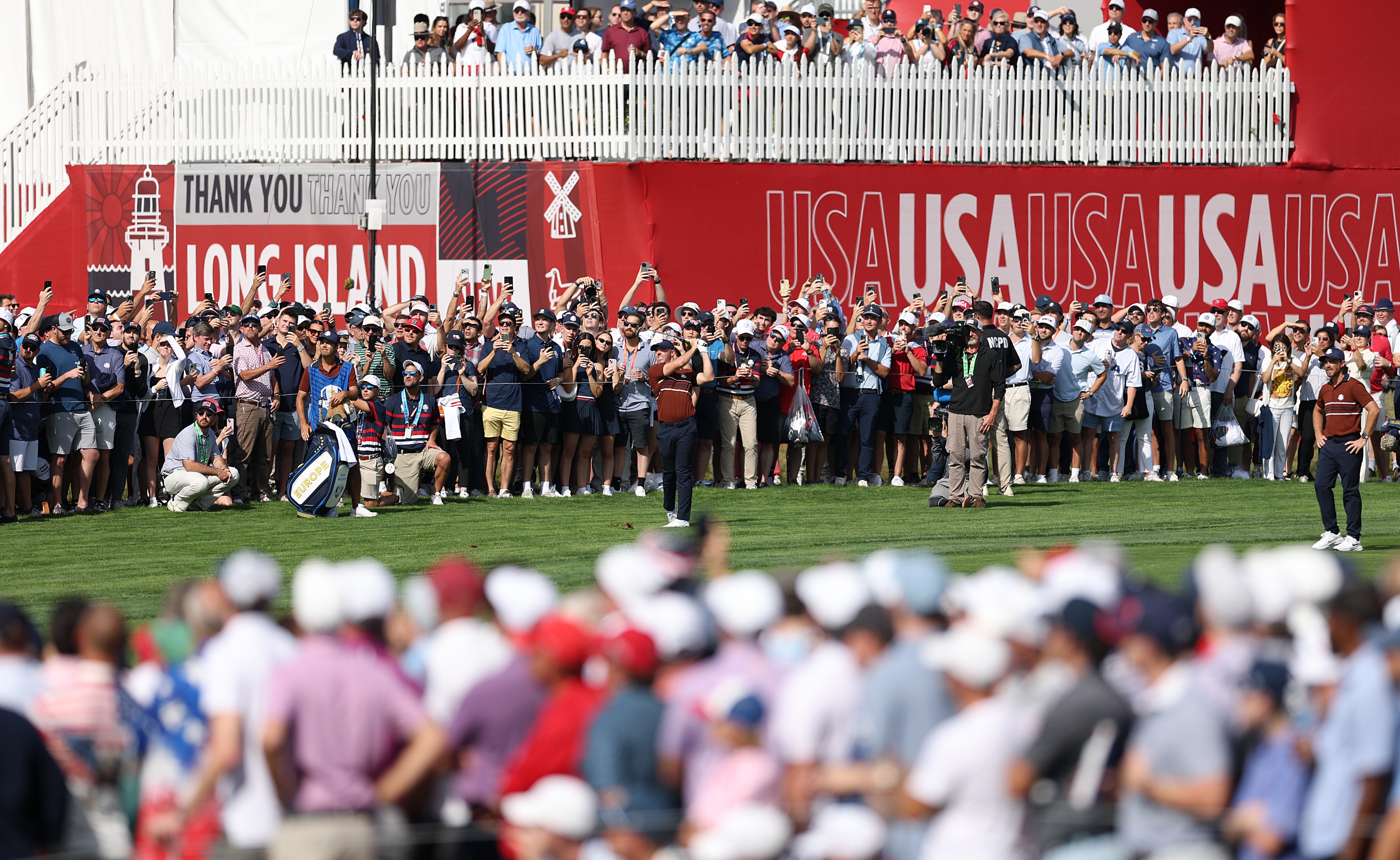 Crowd at a golf event on Long Island, with banners saying "USA" and "Thank you," watching players on the course