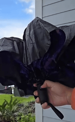 Person demonstrating a reverse-folding umbrella adjacent   a location   exterior