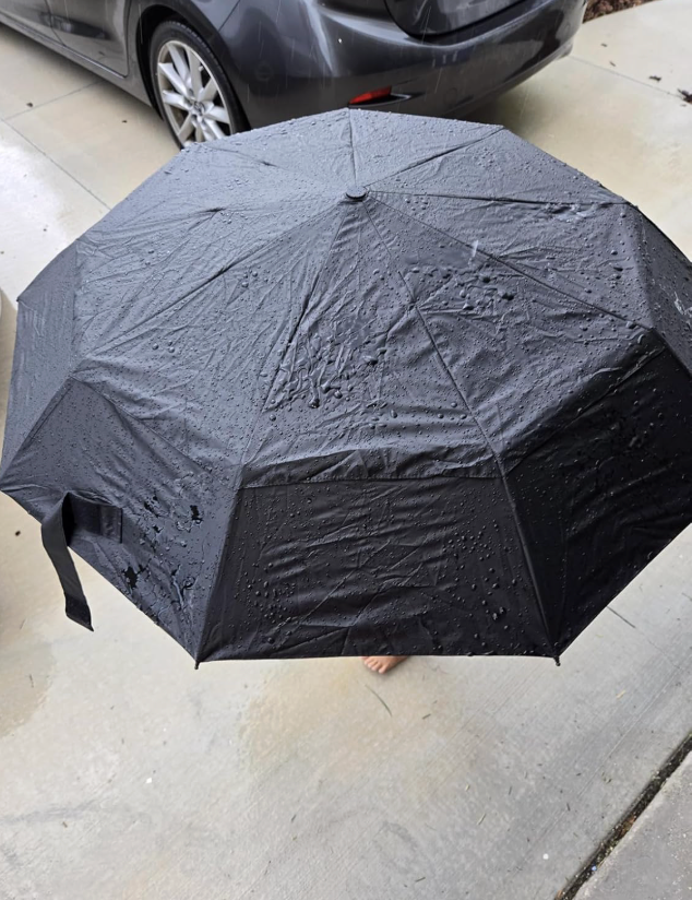 A achromatic  umbrella with rainfall  droplets connected  it is unfastened  connected  a sidewalk adjacent   a parked car