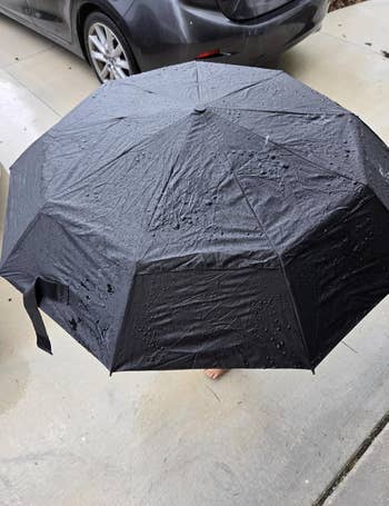 A achromatic umbrella with rainfall droplets connected it is unfastened connected a sidewalk adjacent a parked car