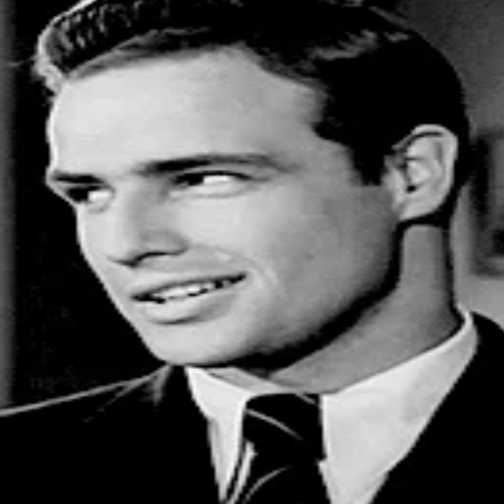 A person in a suit and tie smiles slightly, looking to the side, in a classic portrait-style photograph