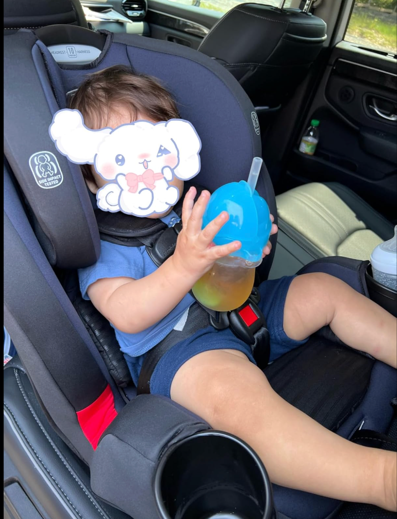 Baby successful  a car   spot   holding a sippy cup, look   partially covered by a cartoon sticker