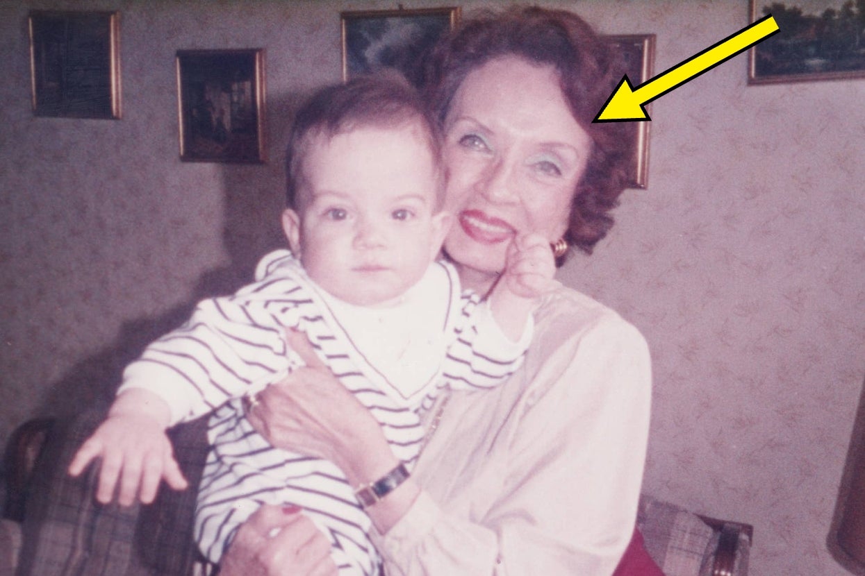 A woman smiles while holding a baby dressed in a striped outfit. A yellow arrow points to the woman, highlighting her