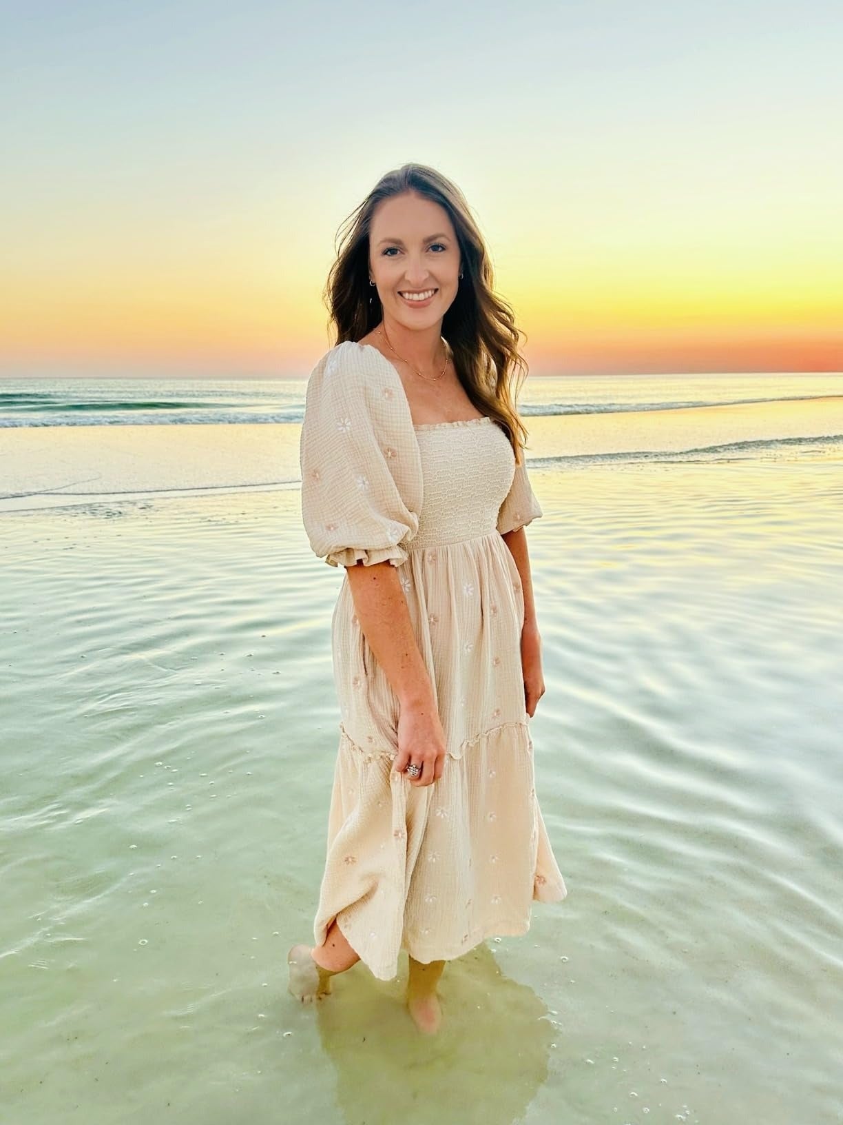 A reviewer stands successful  shallow h2o  astatine  the formation  during sunset, wearing a casual, flowy dress