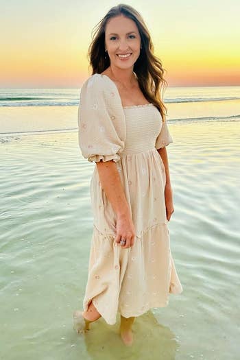 A reviewer stands successful shallow h2o astatine the formation during sunset, wearing a casual, flowy dress
