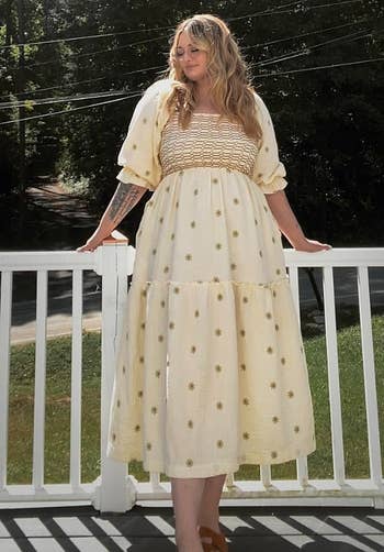 Person successful a light, flowing formal with floral patterns stands connected a structure overlooking a tree-lined area