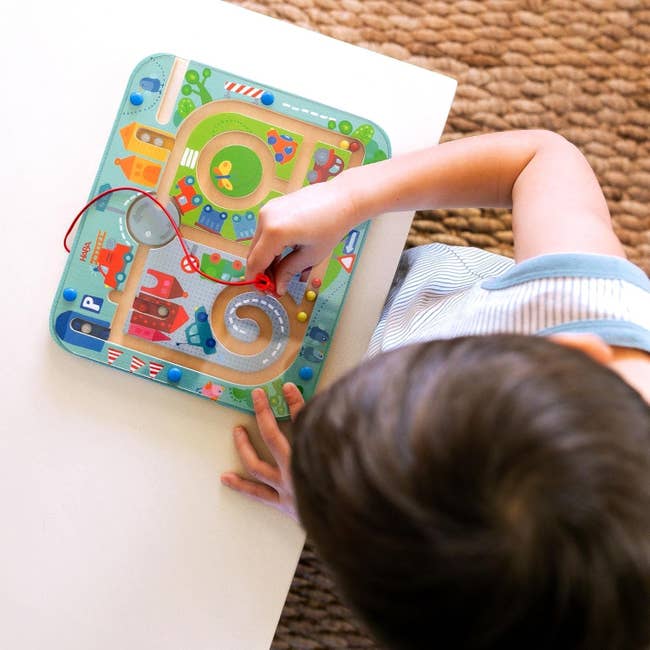 Child playing with a magnetic maze artifact  featuring roads and colorful vehicles