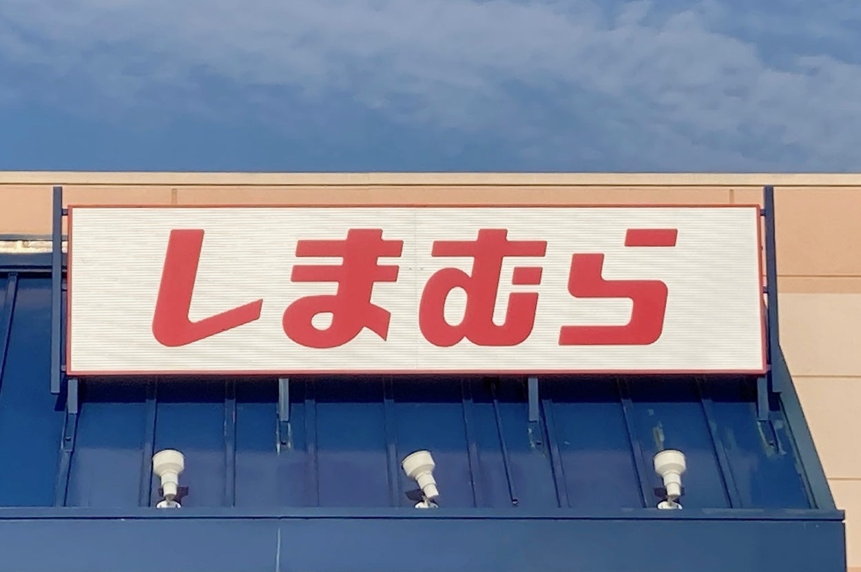 Sign on a building's roof with large Japanese characters, reading "Shimamura." Blue sky in the background
