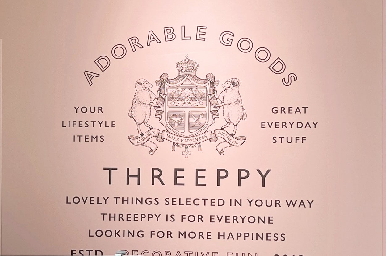 壁に「ADORABLE GOODS THREEPPY GREAT EVERYDAY STUFF」と書かれており、装飾されたエンブレムが描かれている。