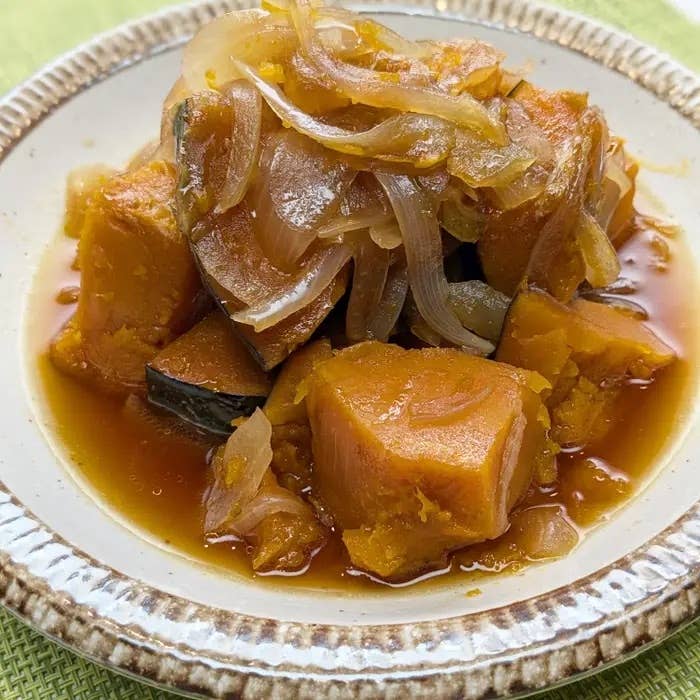 煮物の料理が白い皿に盛られている。かぼちゃと玉ねぎがしょうゆベースのタレと一緒に煮込まれている。