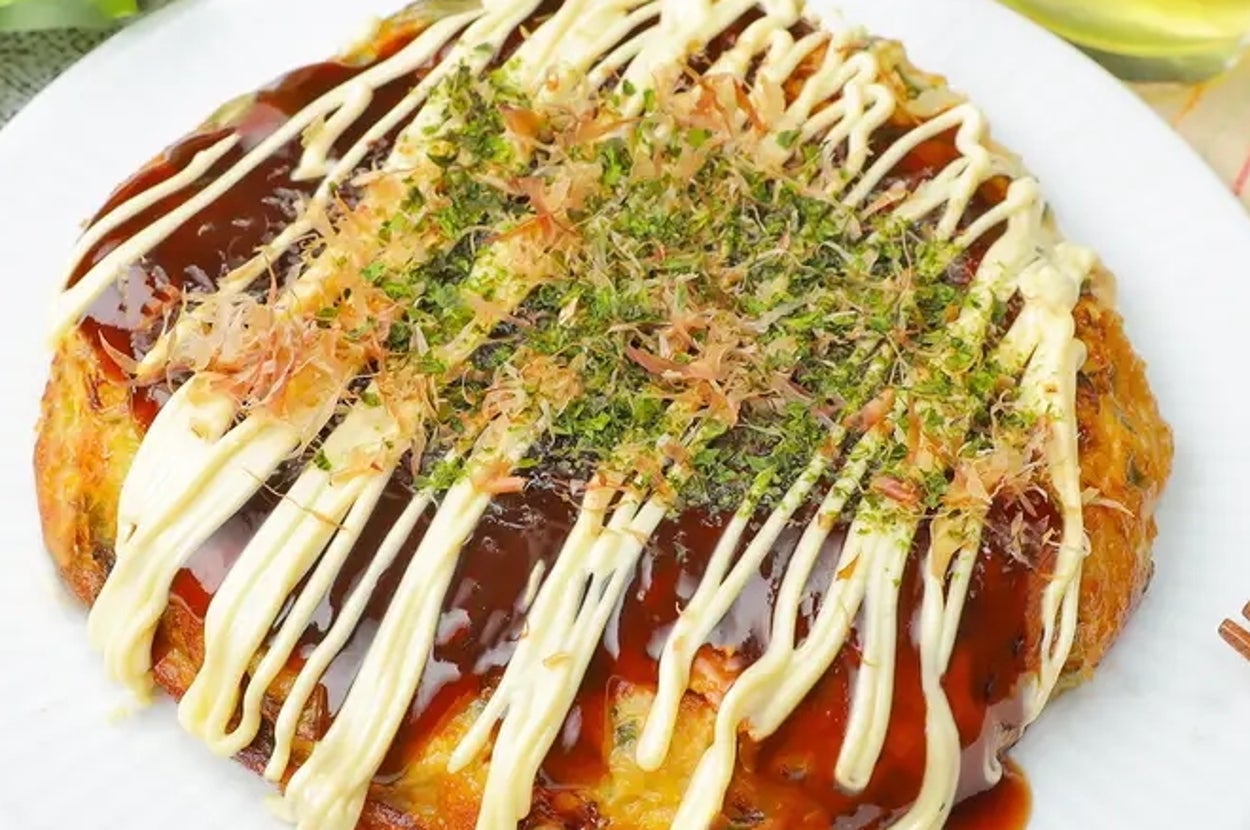 長ねぎとツナのお好み焼きが皿にのっている。上にマヨネーズ、ソース、青のり、かつお節がかかっている。背景には飲み物がある。