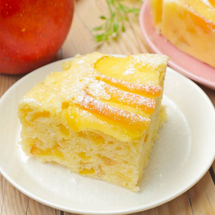 リンゴのスライスがトッピングされた、パウダーシュガーがかかったふんわりとしたケーキが白い皿に載っている。