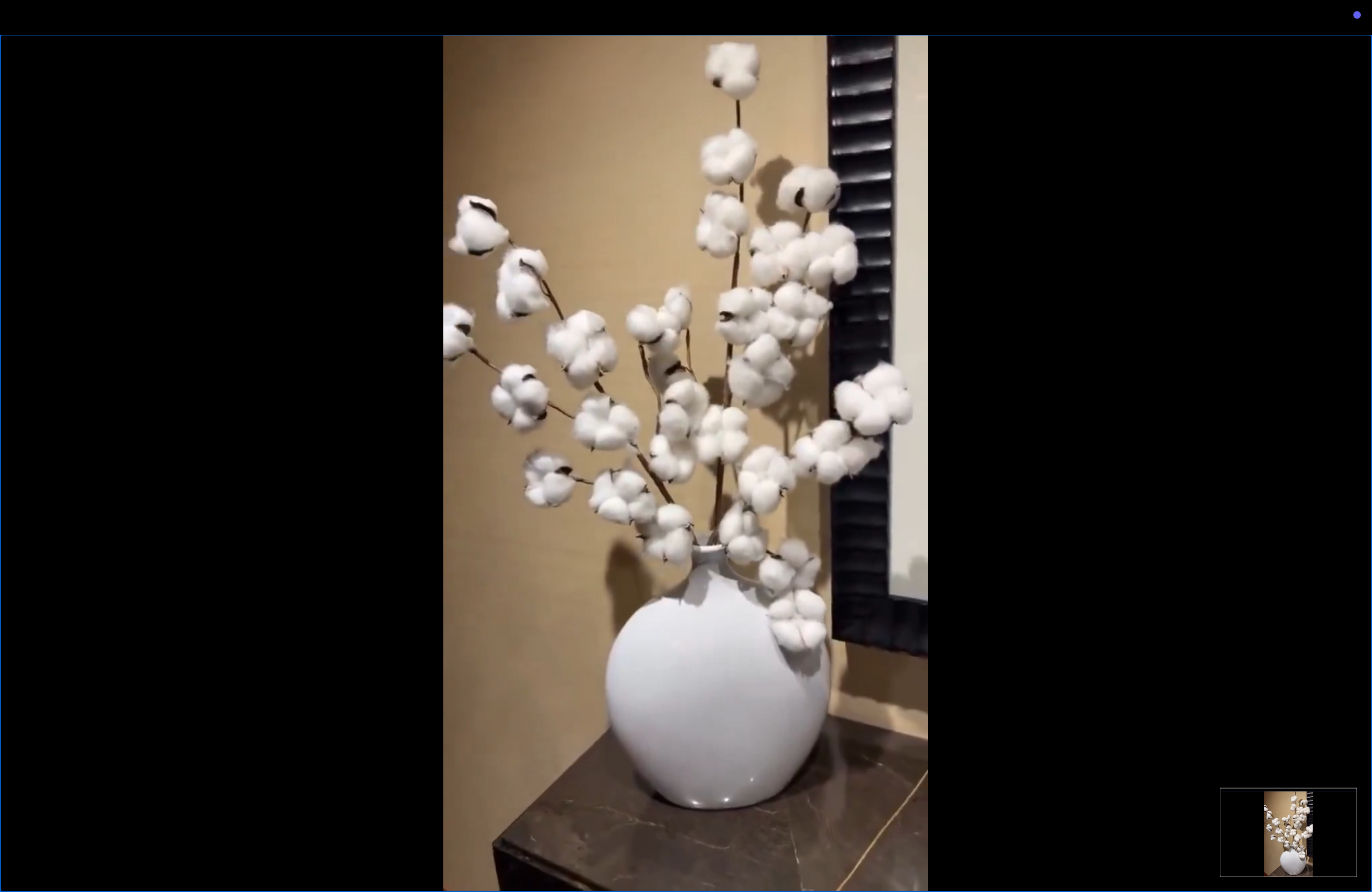 Vase with cotton branches displayed on a table, set against a neutral background