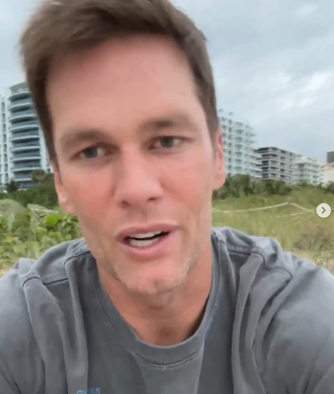 Person outdoors, wearing a casual T-shirt, with modern buildings in the background