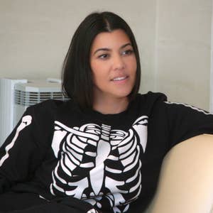 A person is sitting on a beige chair, wearing a casual outfit with a skeleton design on the top