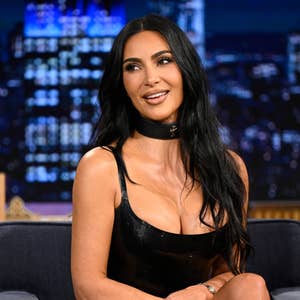 Person in a black leather dress sits on a talk show set, smiling during an interview