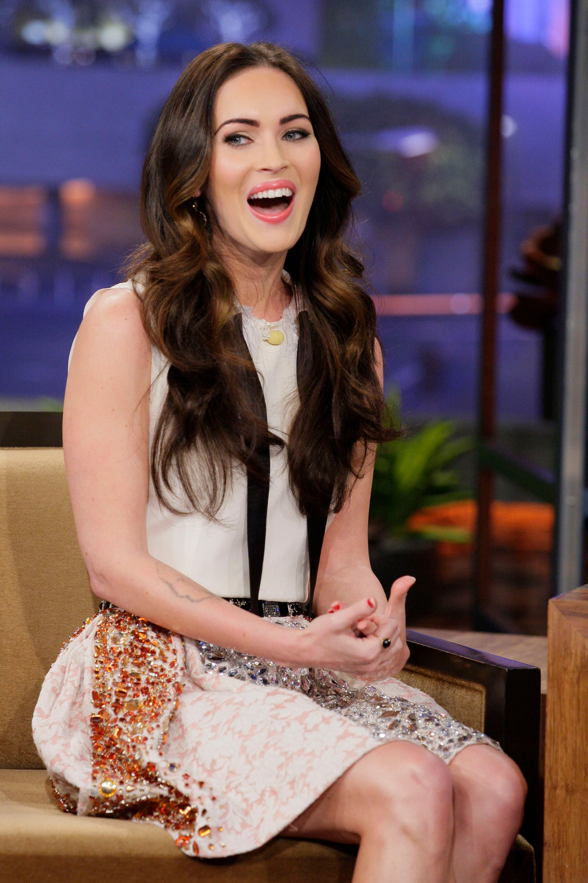 Person smiling and seated during a talk show interview, wearing a sleeveless dress with sequin details