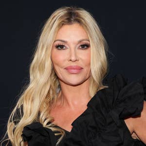 Person with long wavy hair wears an elegant dress with ruffled shoulder detail, posing at a celebrity event