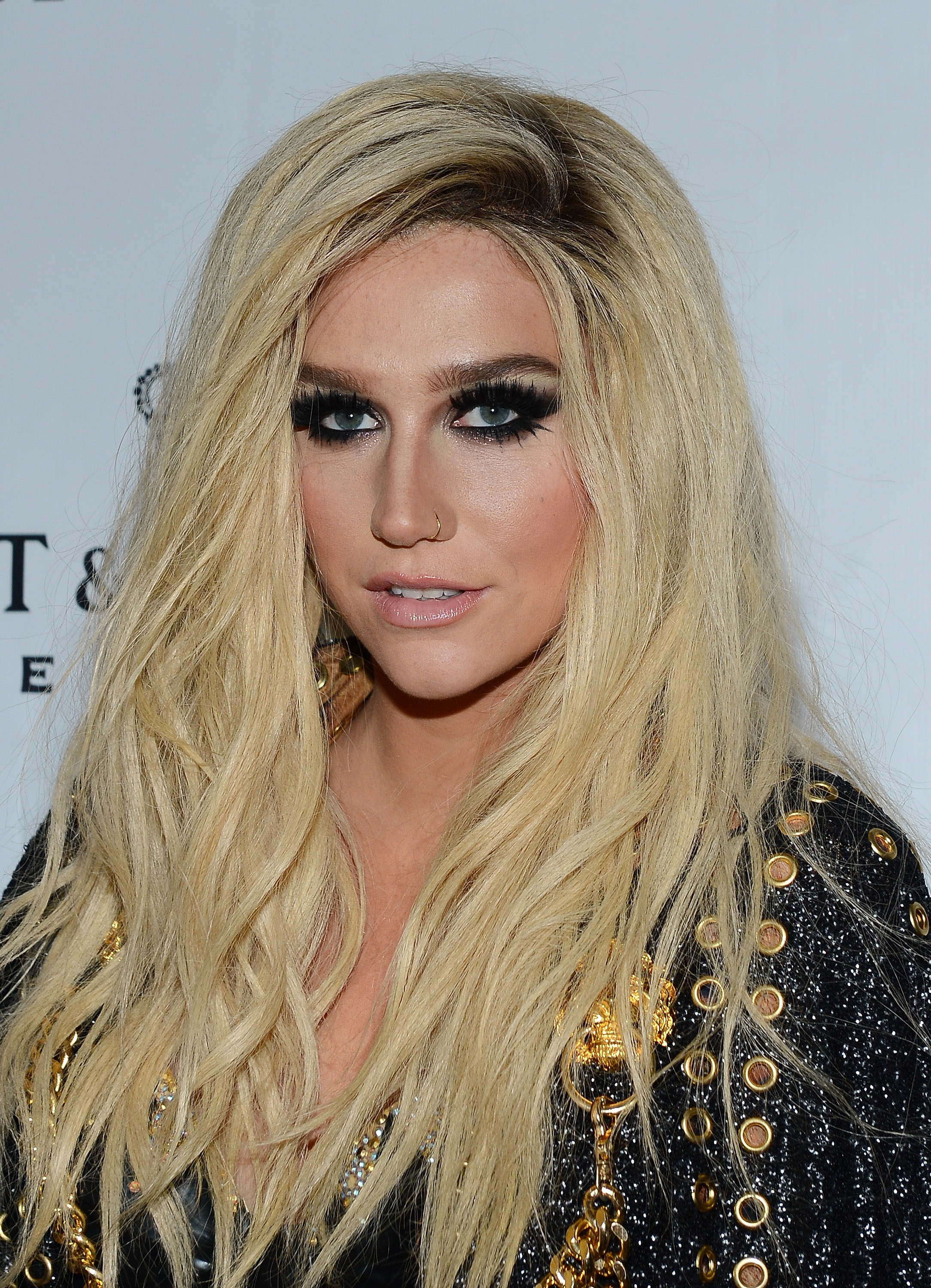 Person with long wavy hair and smoky eye makeup wearing a black outfit with gold embellishments on a red carpet
