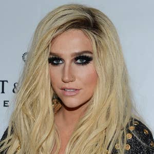 Person with long wavy hair and smoky eye makeup wearing a black outfit with gold embellishments on a red carpet