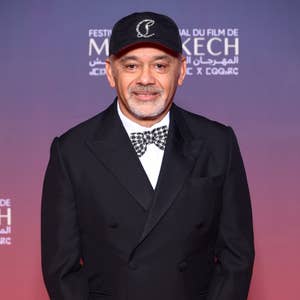 Man in a tailored black suit with a checkered bow tie and black cap, poses on a red carpet at a film festival event