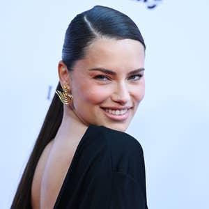 Person with sleek hairstyle and elegant earrings smiling at an event, wearing a chic gown