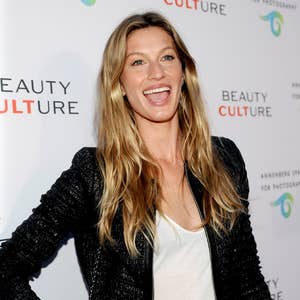 Person smiling on the red carpet in a casual jacket and top, posing for photographers at a Beauty Culture event backdrop