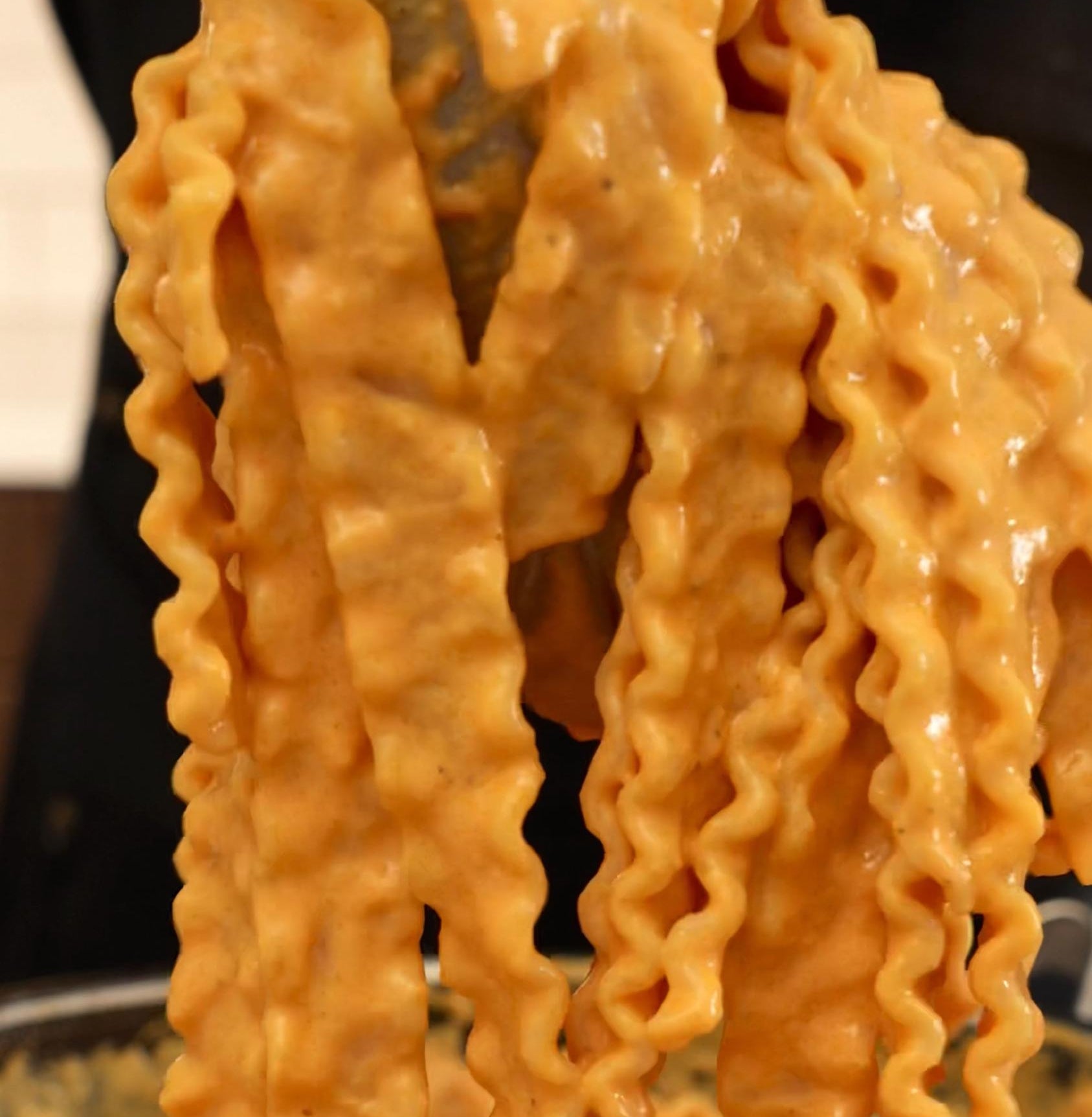 Close-up of wavy pasta coated in creamy sauce being lifted by a spoon, emphasizing rich texture and appetizing appearance