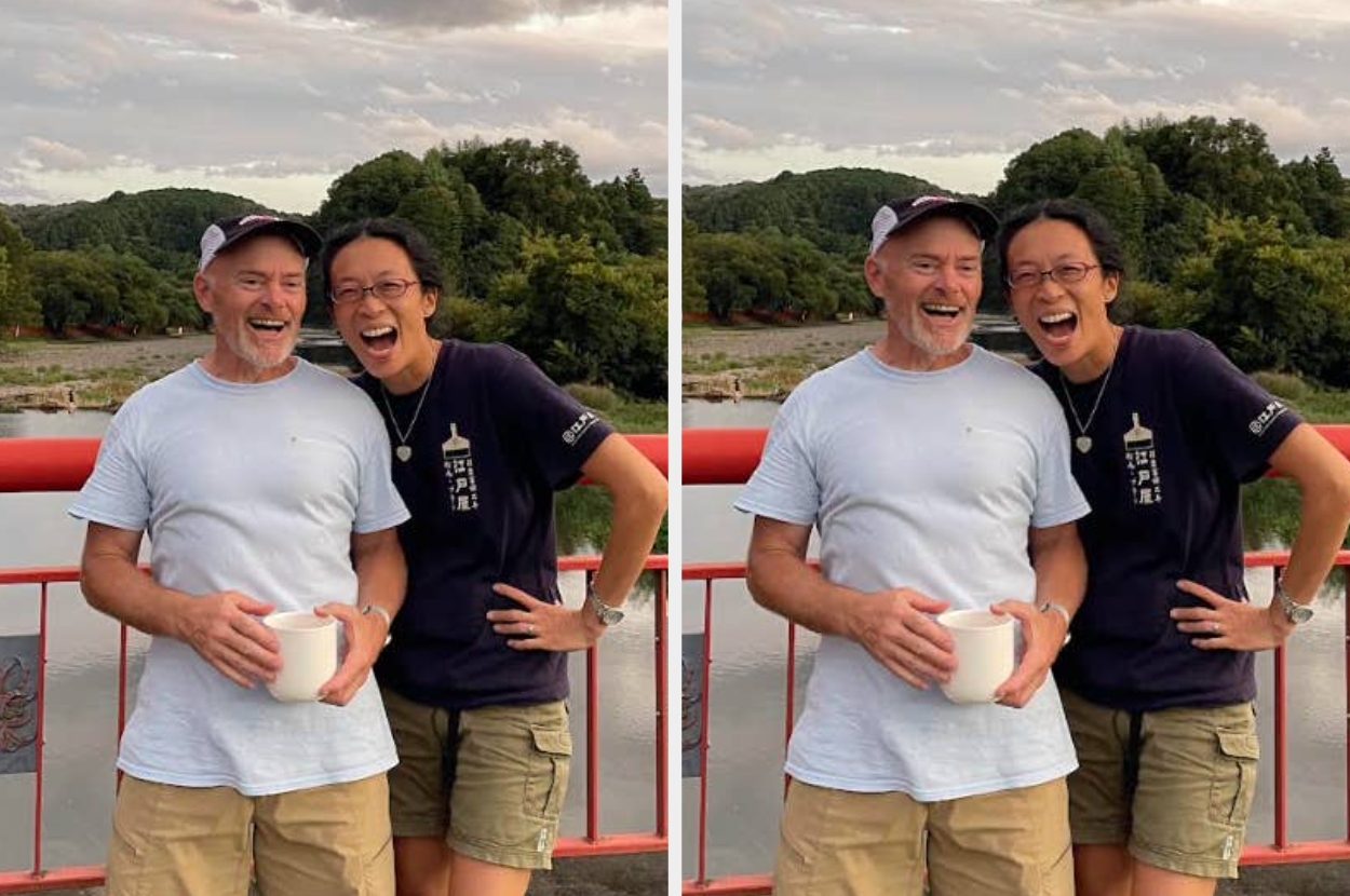 Two people laughing together on a bridge with a scenic background. One holds a mug, both are casually dressed