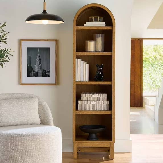 Modern surviving  country   with a gangly  woody  bookshelf holding books and decorative items beside a cozy armchair, framed art, and a pendant lamp