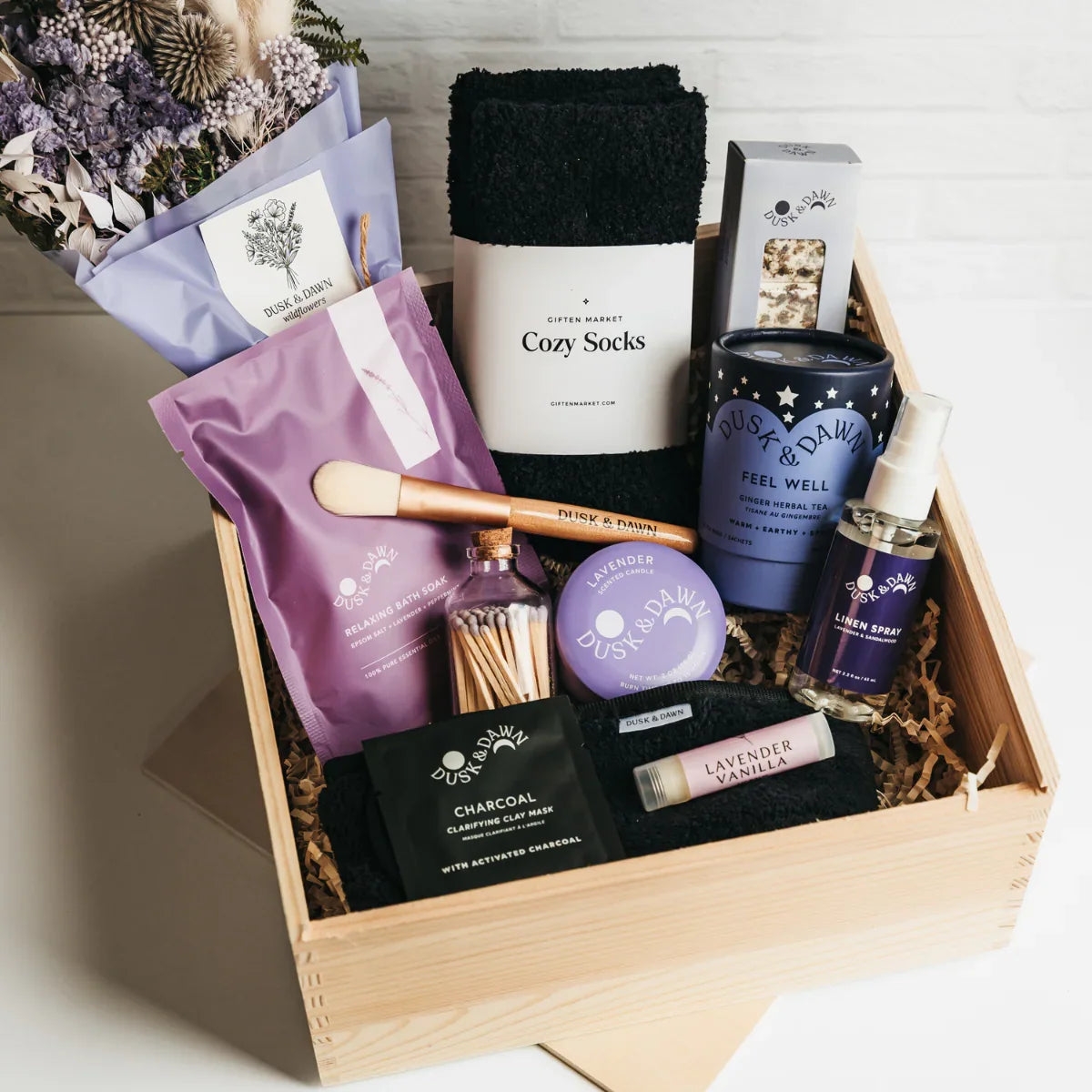 Gift box with self-care items: cozy socks, charcoal soap, face brush, lavender balm, and a scented candle. Perfect for relaxation and pampering