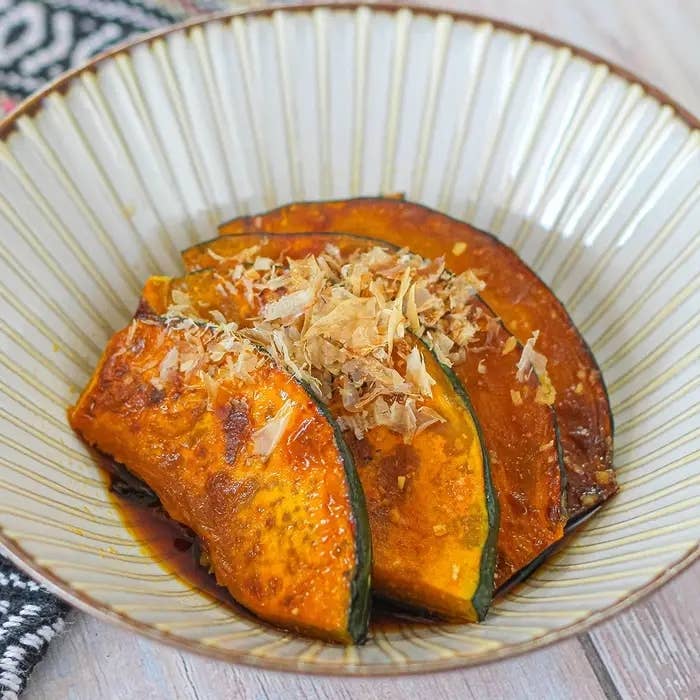 お皿に盛り付けられたかぼちゃの煮物、鰹節が上に乗っている。