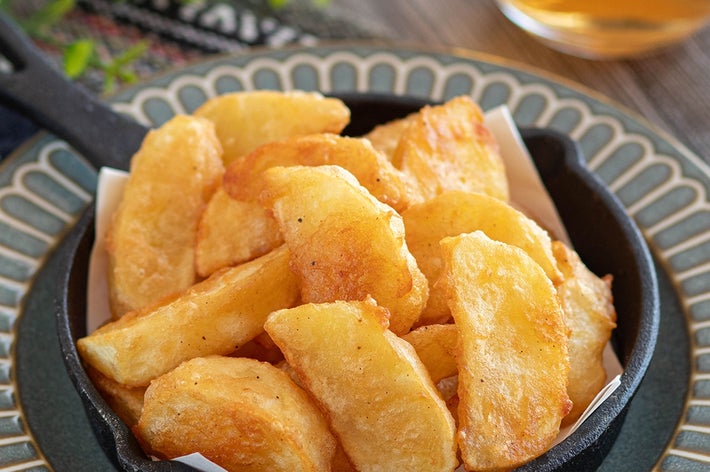 小さなフライパンに盛られた揚げたてのポテトウェッジ。背景に飲み物が見える。