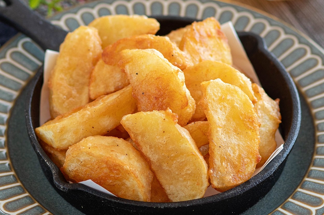 小さなフライパンに盛られた揚げたてのポテトウェッジ。背景に飲み物が見える。