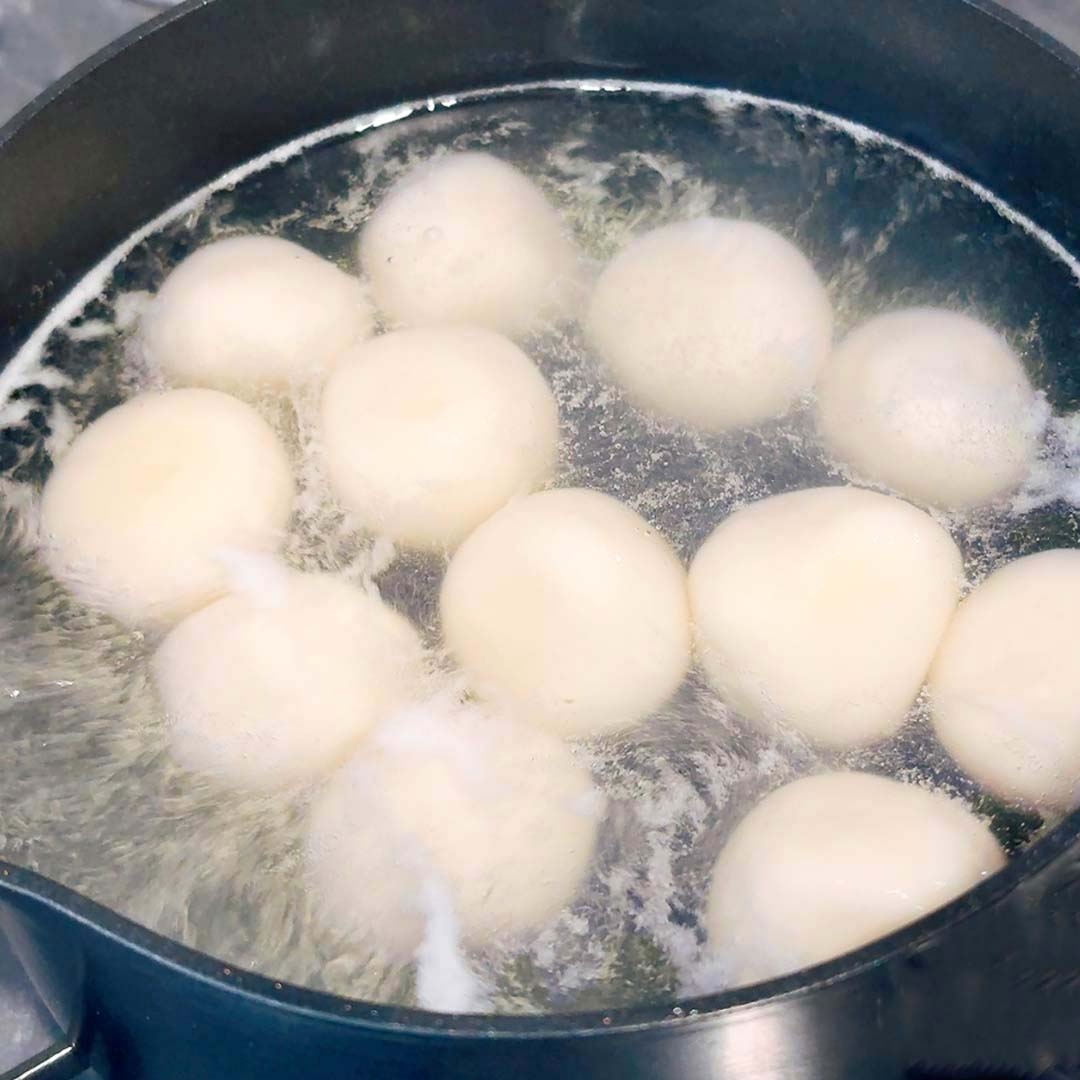 鍋で茹でられている複数の白い団子。泡が立ち上がる中、均等に並んでいる。
