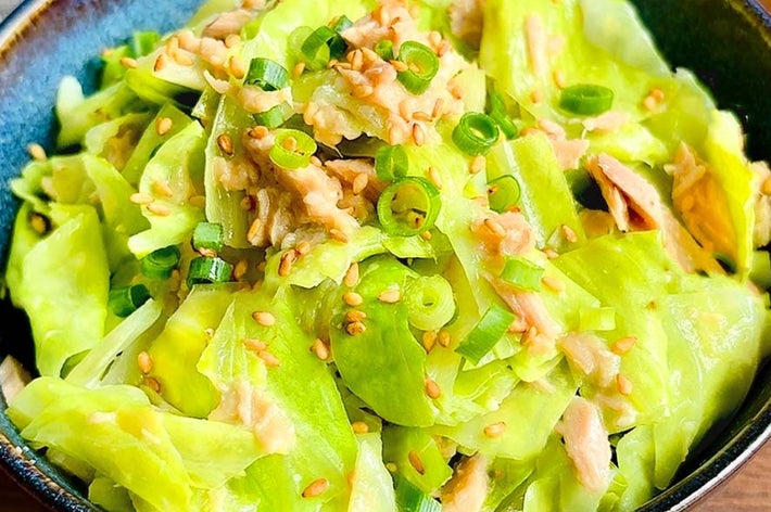 キャベツとチキンのサラダが青いボウルに盛り付けられている。上にネギとゴマがトッピングされている。