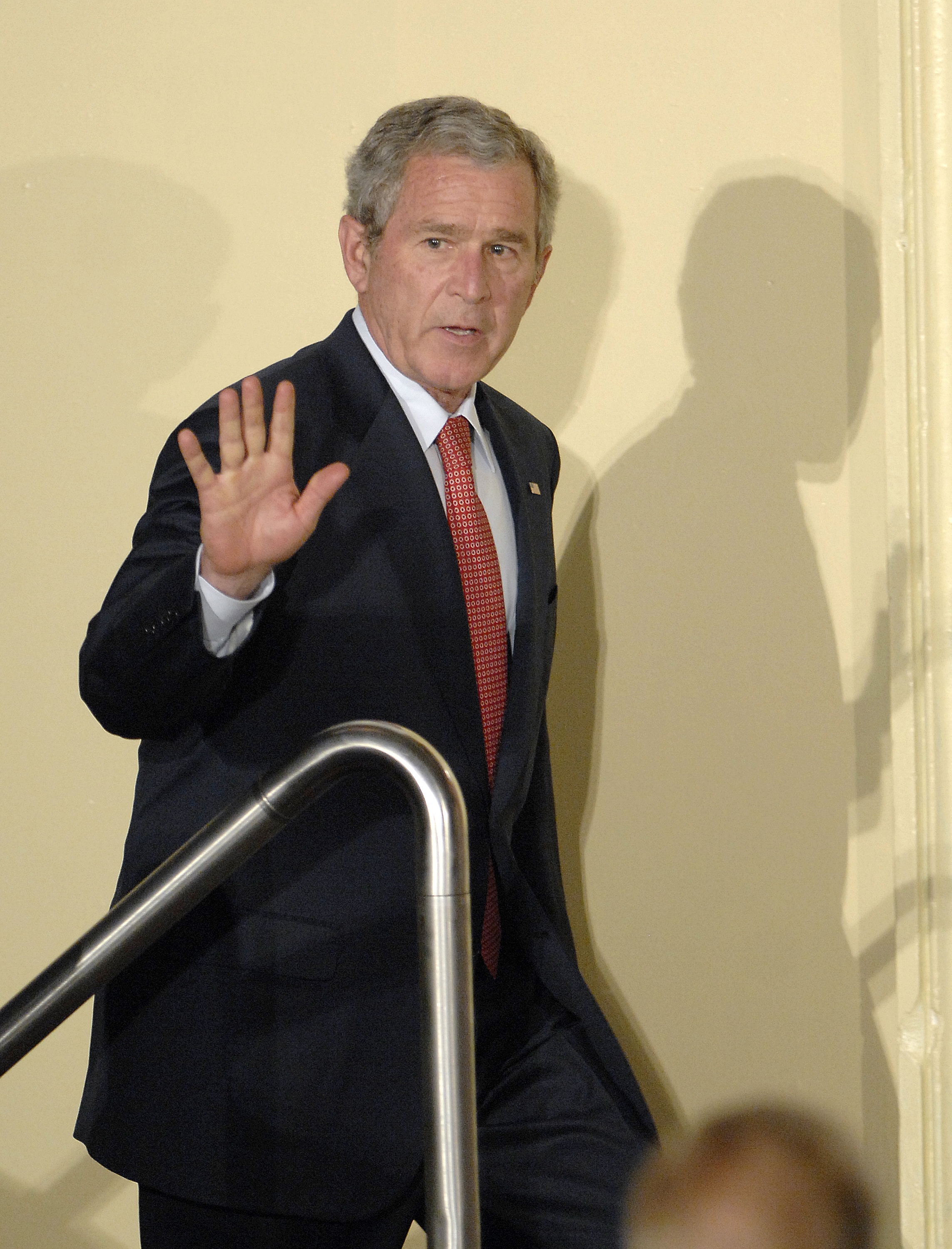 George W Bush waves with 1 manus portion descending stairs, appearing astatine a ceremonial lawsuit oregon property gathering