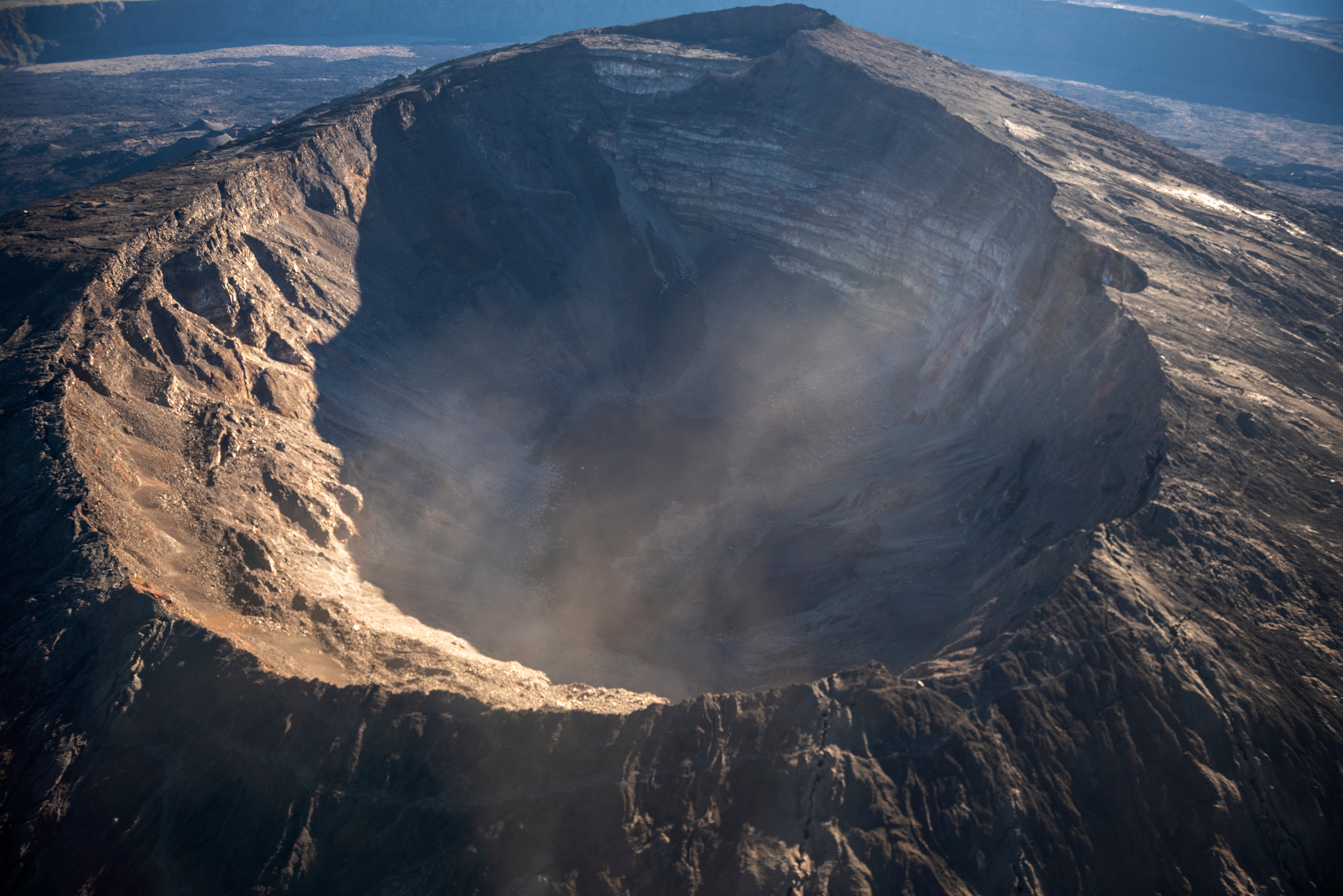 Aerial presumption of a ample volcanic crater with rugged edges and fume oregon mist rising from its center. Surrounding scenery is rocky and barren