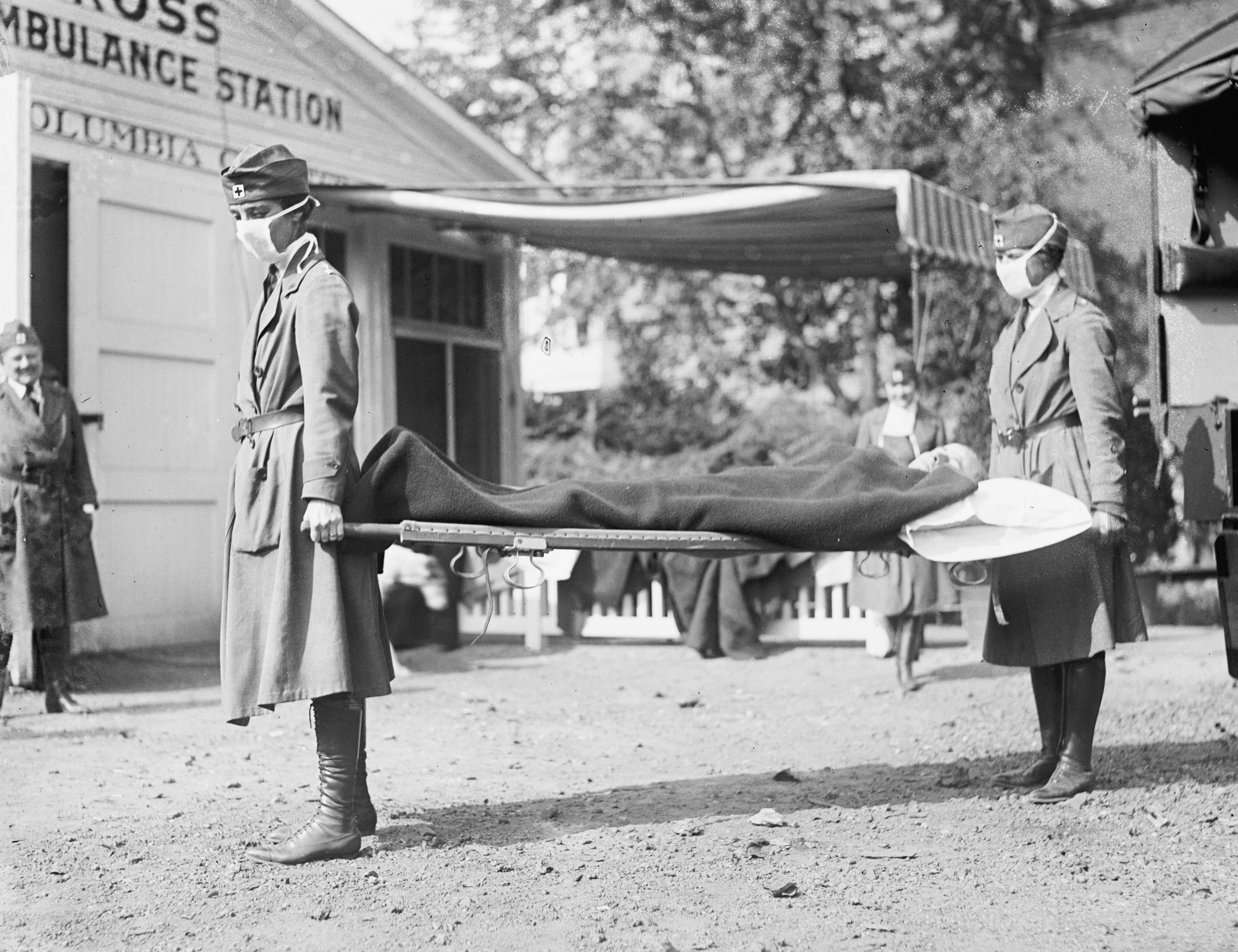 Historical photograph of 2 masked Red Cross nurses carrying a diligent connected a stretcher extracurricular an ambulance presumption during a past pandemic