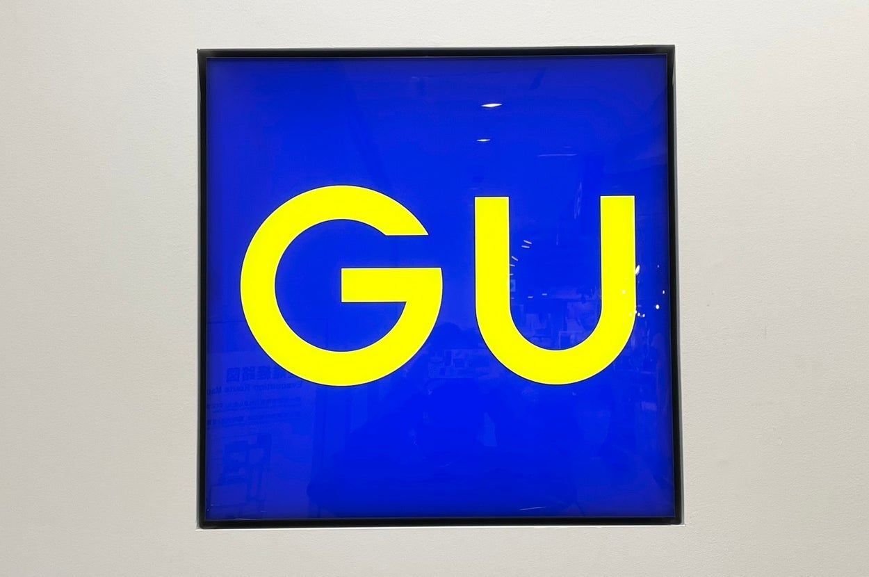A square sign with large letters "GU" in a simple font centered on it