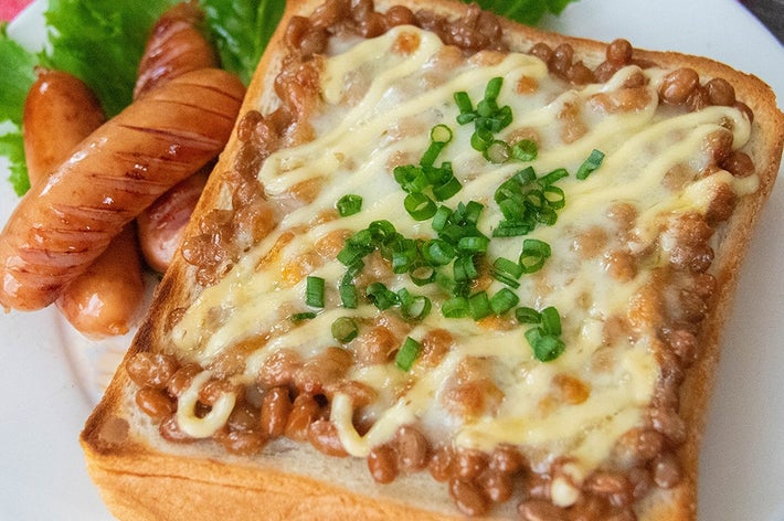 納豆トーストにチーズとマヨネーズ、刻んだ小ネギがのり、ソーセージとレタスが添えられた朝食プレート。