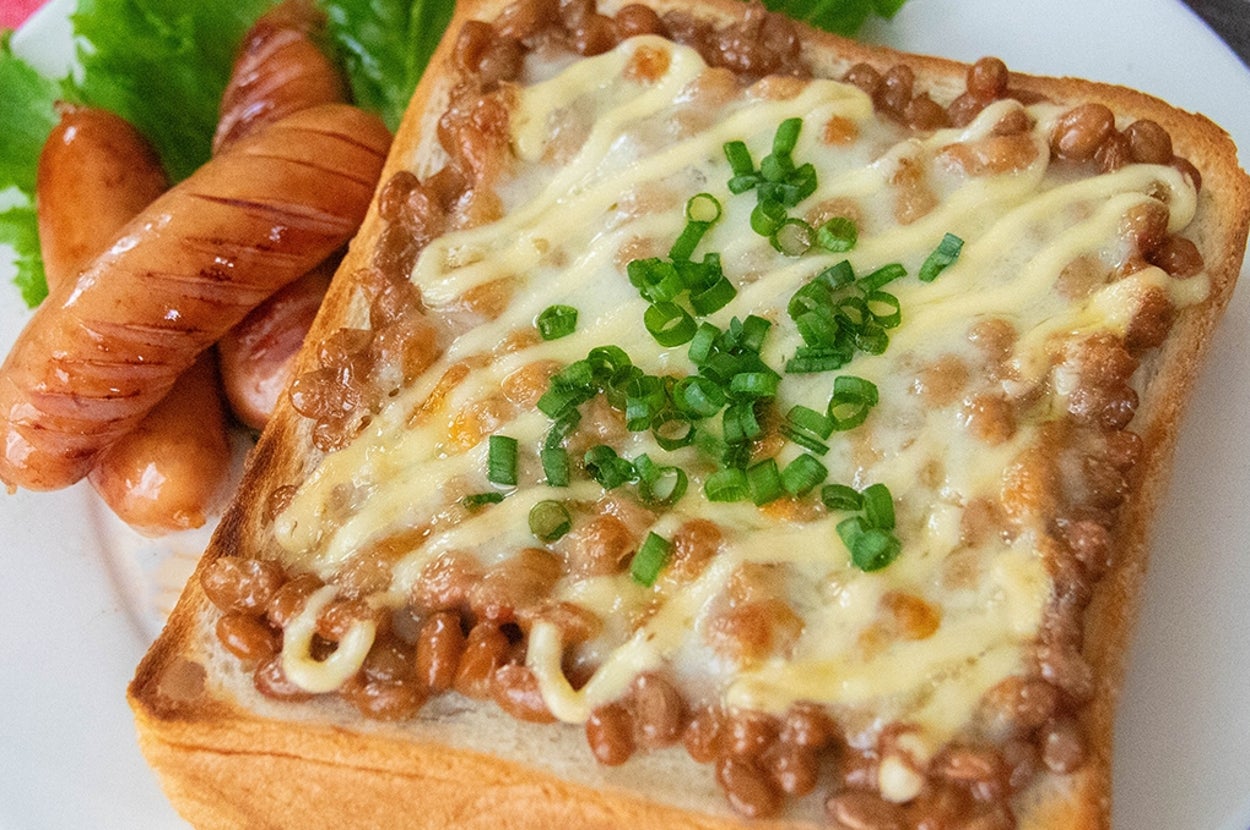 納豆トーストにチーズとマヨネーズ、刻んだ小ネギがのり、ソーセージとレタスが添えられた朝食プレート。