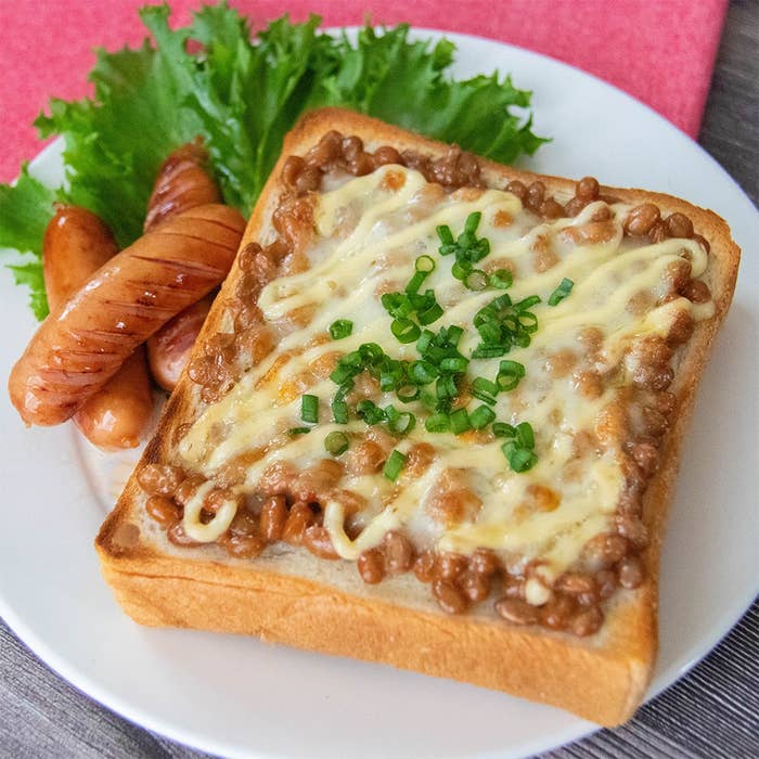 納豆トーストにチーズとマヨネーズ、刻んだ小ネギがのり、ソーセージとレタスが添えられた朝食プレート。