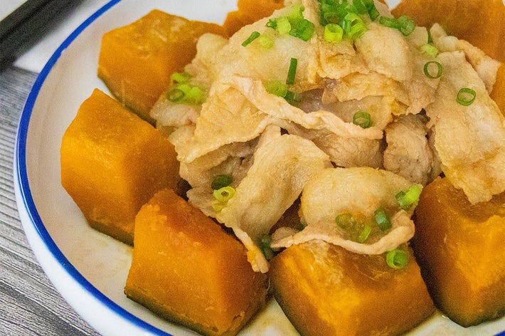 かぼちゃと豚肉の煮物が皿に盛られている。上には刻んだ小ネギがトッピングされ、箸が添えられている。