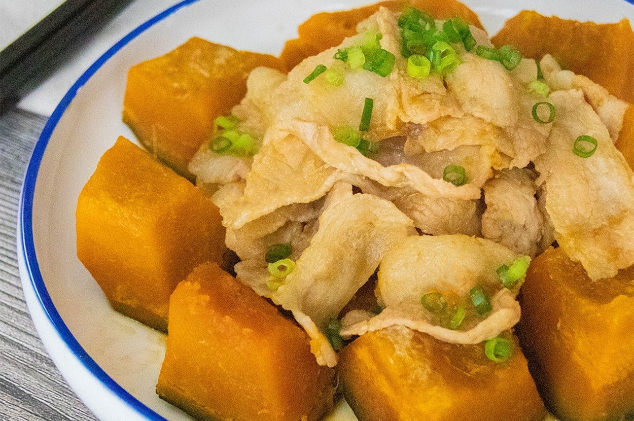 かぼちゃと豚肉の煮物が皿に盛られている。上には刻んだ小ネギがトッピングされ、箸が添えられている。