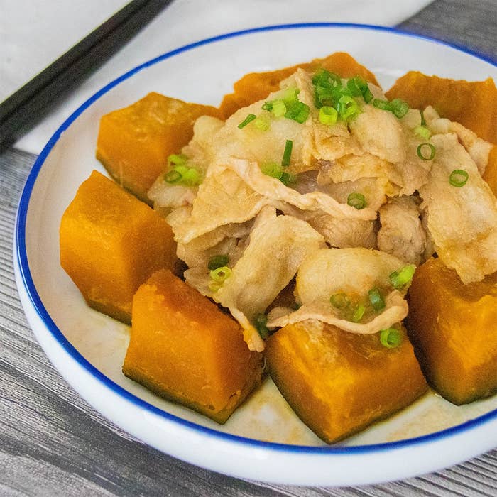 かぼちゃと豚肉の煮物が皿に盛られている。上には刻んだ小ネギがトッピングされ、箸が添えられている。