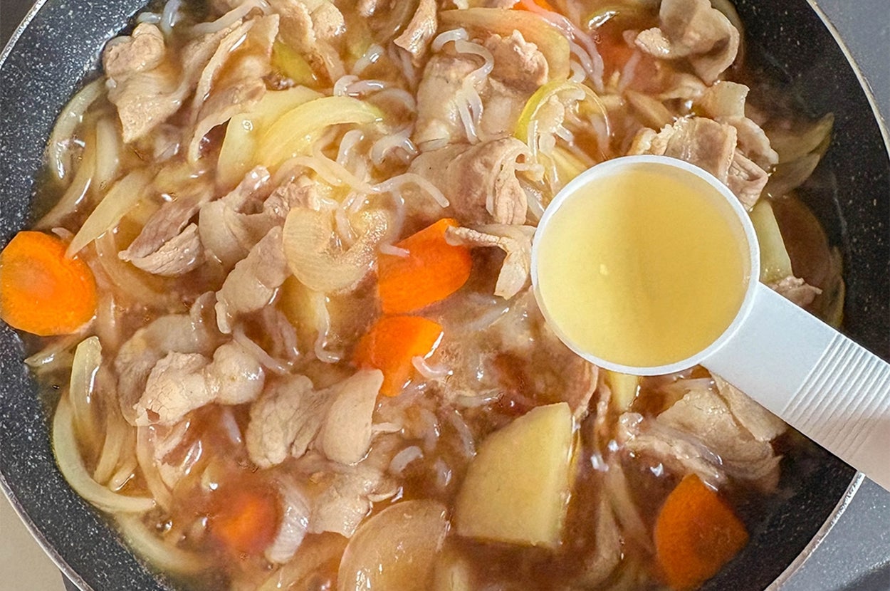 肉じゃがを作る鍋。じゃがいも、玉ねぎ、にんじん、しらたきと豚肉が見え、酢を追加している様子。